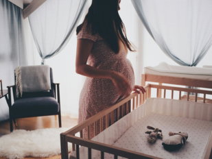 A pregnant woman standing by a wooden crib in a sunlit nursery